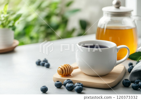 Tea setup with a white cup of blueberry tea, honey dipper, blueberries, and a teapot 120373332