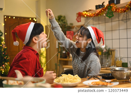 Cheerful young couple having fun sharing spaghetti in a festively decorated kitchen Cheerful young couple having fun sharing spaghetti in a festively decorated kitchen 120373449