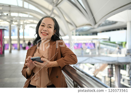 Cheerful mature businesswoman using smartphone in modern urban area Cheerful mature businesswoman using smartphone in modern urban area 120373561