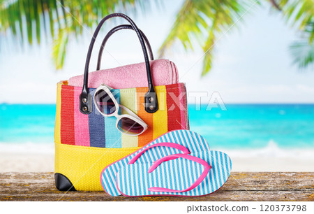 A beach bag with towels, sunglasses, and flip flops placed on a table A beach bag with towels, sunglasses, and flip flops placed on a table 120373798