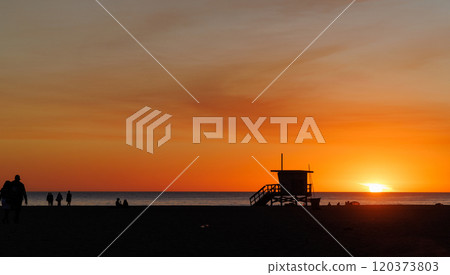 Los Angeles beach at sunset, featuring a lifeguard tower silhouette against a glowing orange and purple horizon 120373803