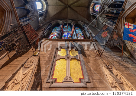 The Chancel of St. Patrick's Cathedral in Dublin features a large mosaic cross, flanked by military regimental flags and stone carvings. Above, the gothic stained glass windows add a solemn atmosphere The Chancel of St. Patrick's Cathedral in Dublin features a large mosaic cross, flanked by military regimental flags and stone carvings. Above, the gothic stained glass windows add a solemn atmosphere 120374181