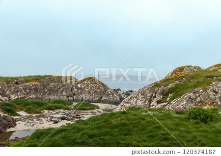 Coastal landscape of Coral Strand Beach, Connemara, Ireland, showcasing rugged rocks and lush green hills leading down to a fog-shrouded sea Coastal landscape of Coral Strand Beach, Connemara, Ireland, showcasing rugged rocks and lush green hills leading down to a fog-shrouded sea 120374187
