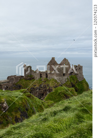 Historic Dunluce Castle above steep cliffs with cloudy sky creating an atmospheric view Historic Dunluce Castle above steep cliffs with cloudy sky creating an atmospheric view 120374213