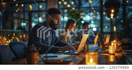 Modern office workers staying late, illuminated by warm candlelight and bokeh. Young professionals focused on laptops in contemporary coworking space with atmospheric evening lighting Modern office workers staying late, illuminated by warm candlelight and bokeh. Young professionals focused on laptops in contemporary coworking space with atmospheric evening lighting 120374989