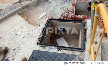 Construction work is taking place on a street where a drainage system is being installed alongside communication lines. Materials and tools are scattered around as workers progress. 120375480