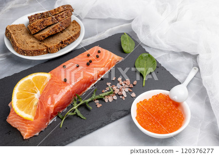 Fillet of raw salmon fish with arugula, basil and lemon on the cutting board with red caviar. Fillet of raw salmon fish with arugula, basil and lemon on the cutting board with red caviar. 120376277