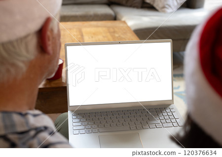 Senior couple wearing Santa hats using laptop at home during Christmas, copy space Senior couple wearing Santa hats using laptop at home during Christmas, copy space 120376634