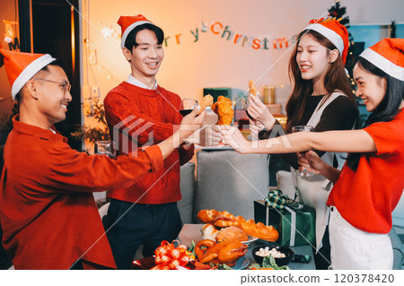 Group of young Asian man and women as friends having fun at a New Year's celebration, holding gift boxes standing by Christmas tree decoration, midnight countdown Party at home with holiday season. 120378420