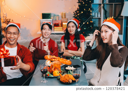 Group of young Asian man and women as friends having fun at a New Year's celebration, holding gift boxes standing by Christmas tree decoration, midnight countdown Party at home with holiday season. Group of young Asian man and women as friends having fun at a New Year's celebration, holding gift boxes standing by Christmas tree decoration, midnight countdown Party at home with holiday season. 120378421