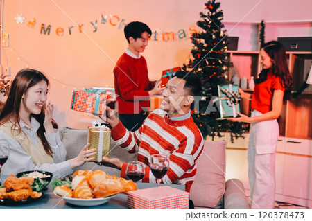 Friends opening Christmas gifts in living room 120378473
