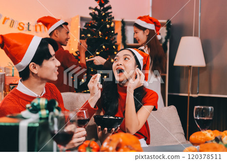Group of young Asian man and women as friends having fun at a New Year's celebration, holding gift boxes standing by Christmas tree decoration, midnight countdown Party at home with holiday season. 120378511