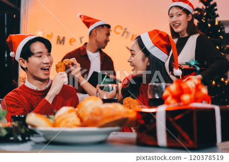Group of young Asian man and women as friends having fun at a New Year's celebration, holding gift boxes standing by Christmas tree decoration, midnight countdown Party at home with holiday season. 120378519