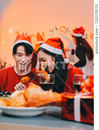 Group of young Asian man and women as friends having fun at a New Year's celebration, holding gift boxes standing by Christmas tree decoration, midnight countdown Party at home with holiday season. 120378520