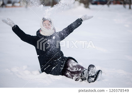 Schoolgirl sitting in the snow throwing snow in the air with arms outstretched, enjoying a winter day Schoolgirl sitting in the snow throwing snow in the air with arms outstretched, enjoying a winter day 120378549