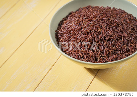 A bowl of red rice is placed on a yellow table close up 120378795
