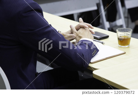 一個穿西裝的男人的手將雙手折疊在長桌上 120379072