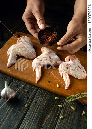 Chef seasons chicken wings with his hands on a cutting board. Preparing to fry poultry wings with spices. Chicken meat diet concept. Asian cuisine Chef seasons chicken wings with his hands on a cutting board. Preparing to fry poultry wings with spices. Chicken meat diet concept. Asian cuisine 120379708