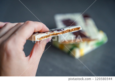 Piece of trend Dubai white chocolate with halva paste in woman hand. Confectionery handmade sweets at home in the kitchen. Piece of trend Dubai white chocolate with halva paste in woman hand. Confectionery handmade sweets at home in the kitchen. 120380344