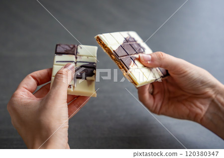 Piece of trend Dubai white chocolate with halva paste in woman hands. Confectionery handmade sweets at home in the kitchen.  120380347