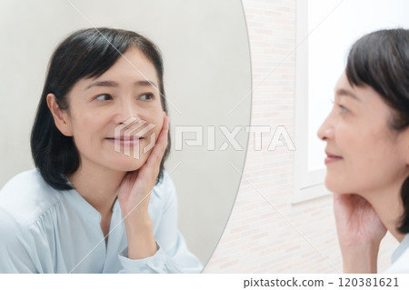 Middle-aged woman looking at the mirror and doing skin care (beauty) 120381621