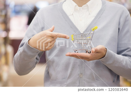 A man's hand pointing at a miniature shopping cart in a supermarket 120381640