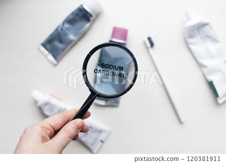 Sodium carbonate in natural toothpaste. Magnifying glass is directed at a tube with a list of ingredients of a safe product. Safe toothpaste composition Sodium carbonate in natural toothpaste. Magnifying glass is directed at a tube with a list of ingredients of a safe product. Safe toothpaste composition 120381911