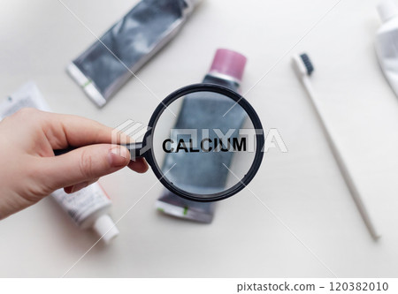 Calcium in natural toothpaste. Magnifying glass is directed at a tube with a list of ingredients of a safe product. Safe toothpaste composition Calcium in natural toothpaste. Magnifying glass is directed at a tube with a list of ingredients of a safe product. Safe toothpaste composition 120382010