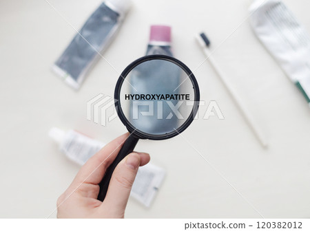 Hydroxyapatite in natural toothpaste. Magnifying glass is directed at a tube with a list of ingredients of a safe product. Safe toothpaste composition 120382012