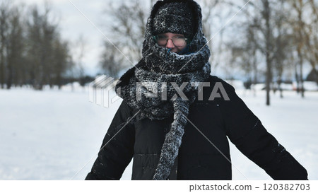 Young girl in a cozy hat and scarf playing in a snowy park on a winter day 120382703