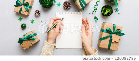 Woman writing Christmas to do list on notebook on colored background with xmas decorations 120382759