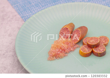 Finger limes served on a blue plate. Cross-section of finger lime and chunks of flesh 120383332