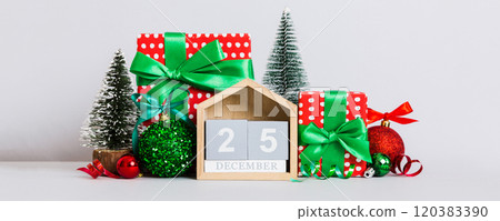 25 december. Christmas composition on colored background with a wooden calendar, with a gift box, toys, bauble copy space 120383390