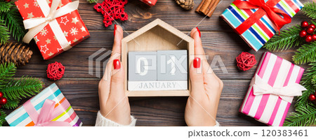 Top view of female hands holding a calendar on wooden background. The first of January. Holiday decorations. New Year concept 120383461