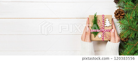 Woman hands give wrapped christmas handmade present in paper with christmas decoration. Present box on holiday on dark wooden table, top view 120383556