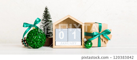 1 january. Christmas composition on colored background with a wooden calendar, with a gift box, toys, bauble copy space 120383842