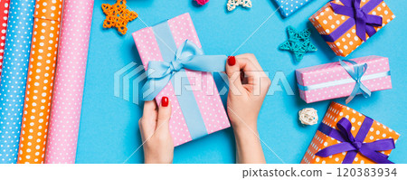 Top view of female hands holding a Christmas present on festive blue background. Holiday decorations and wrapping paper. New Year holiday concept Top view of female hands holding a Christmas present on festive blue background. Holiday decorations and wrapping paper. New Year holiday concept 120383934