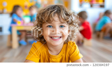 Smiling preschool child with curly hair and bright blue eyes in a cheerful classroom environment, close-up portrait of happy kid showing teeth 120384197