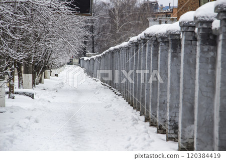 A long grey concrete fence by a snow way in front of an industrial wall of a factory in Ukraine in city Sumy A long grey concrete fence by a snow way in front of an industrial wall of a factory in Ukraine in city Sumy 120384419