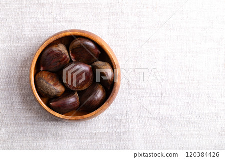 Sweet chestnuts in a wooden bowl on linen, from above, with empty space for text. Castanea sativa, raw, whole and unshelled. Can be eaten raw, candied, cooked, or roasted as a warm snack on streets. Sweet chestnuts in a wooden bowl on linen, from above, with empty space for text. Castanea sativa, raw, whole and unshelled. Can be eaten raw, candied, cooked, or roasted as a warm snack on streets. 120384426