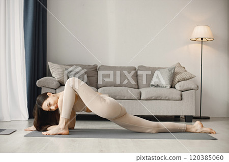 Attractive young woman doing yoga stretching online at home. Brunette woman wearing beige leggins and top. Self-isolation is beneficial, entertainment and education on the Internet. 120385060