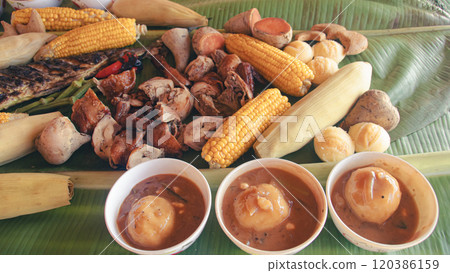 A detailed look at an assortment of grilled vegetable, fish, lechon, chicken,corn and soups served on a banana leaf in a traditional Filipino meal set called boodle fight 120386159