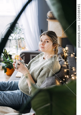 Pregnant woman relaxing at home with a warm cup of tea, embracing a peaceful and cozy living space. Comfort and self-care during pregnancy. 120386491