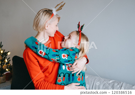 Mother and daughter sharing a playful Christmas moment adjusting festive headbands. Family bonding, holiday fun, Christmas joy, creating memories, festive spirit. 120386516