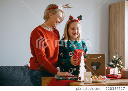 Mother and daughter strengthening family bonds through Christmas gift exchange. Family connection, holiday togetherness, maintaining traditions, Christmas joy, family time. 120386517