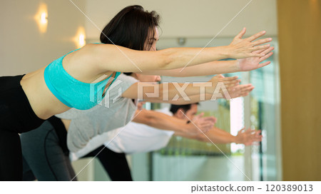 Group of people practicing yoga in indoor fitness room, stretching arms forward in focused balance and concentration posture Group of people practicing yoga in indoor fitness room, stretching arms forward in focused balance and concentration posture 120389013