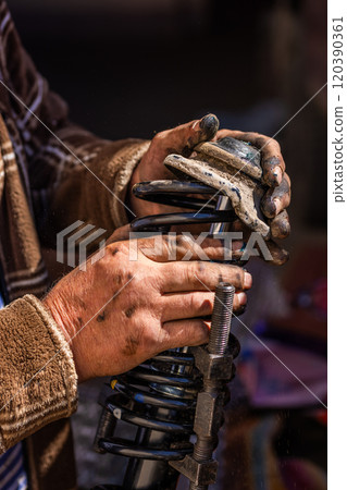 The calloused hands of a mechanic assembling compressed coil spring during DIY car repairs. 120390361