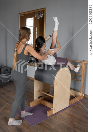 Portrait of woman with pilates trainer doing exersices on the Ladder Barrel. Pilates equipment. Pilates studio machine for fitness workouts in gym. Fit, healthy and strong authentical body. Portrait of woman with pilates trainer doing exersices on the Ladder Barrel. Pilates equipment. Pilates studio machine for fitness workouts in gym. Fit, healthy and strong authentical body. 120390382