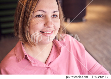 Smiling woman in pink shirt with glitter freckles sitting indoors in soft 120390417