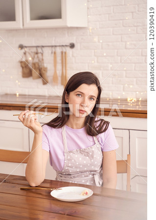 Pensive woman in apron holding chopsticks in minimalist kitchen with string 120390419